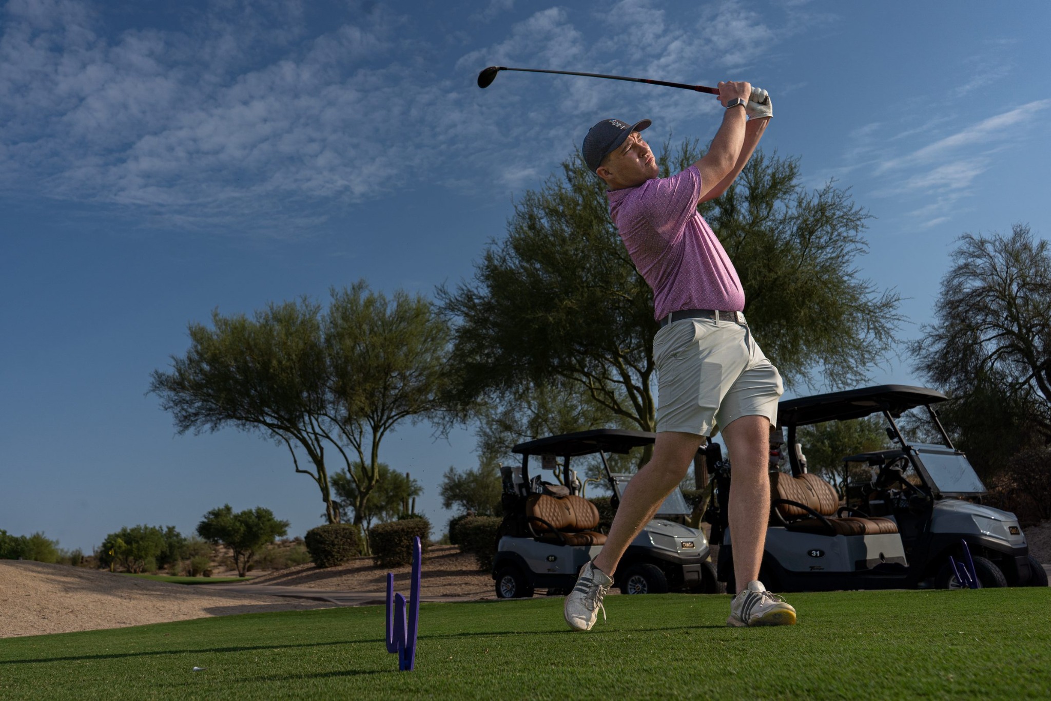 Golfer holding his driver finish on a desert tee box, carts and palo verde trees behind