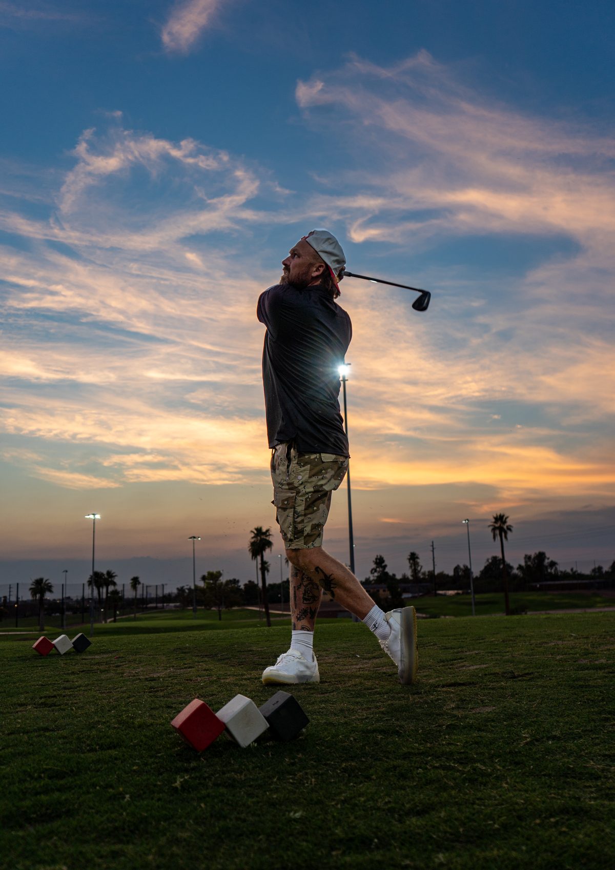 Golfer's follow-through silhouetted against a sunset sky, a course light glowing behind him