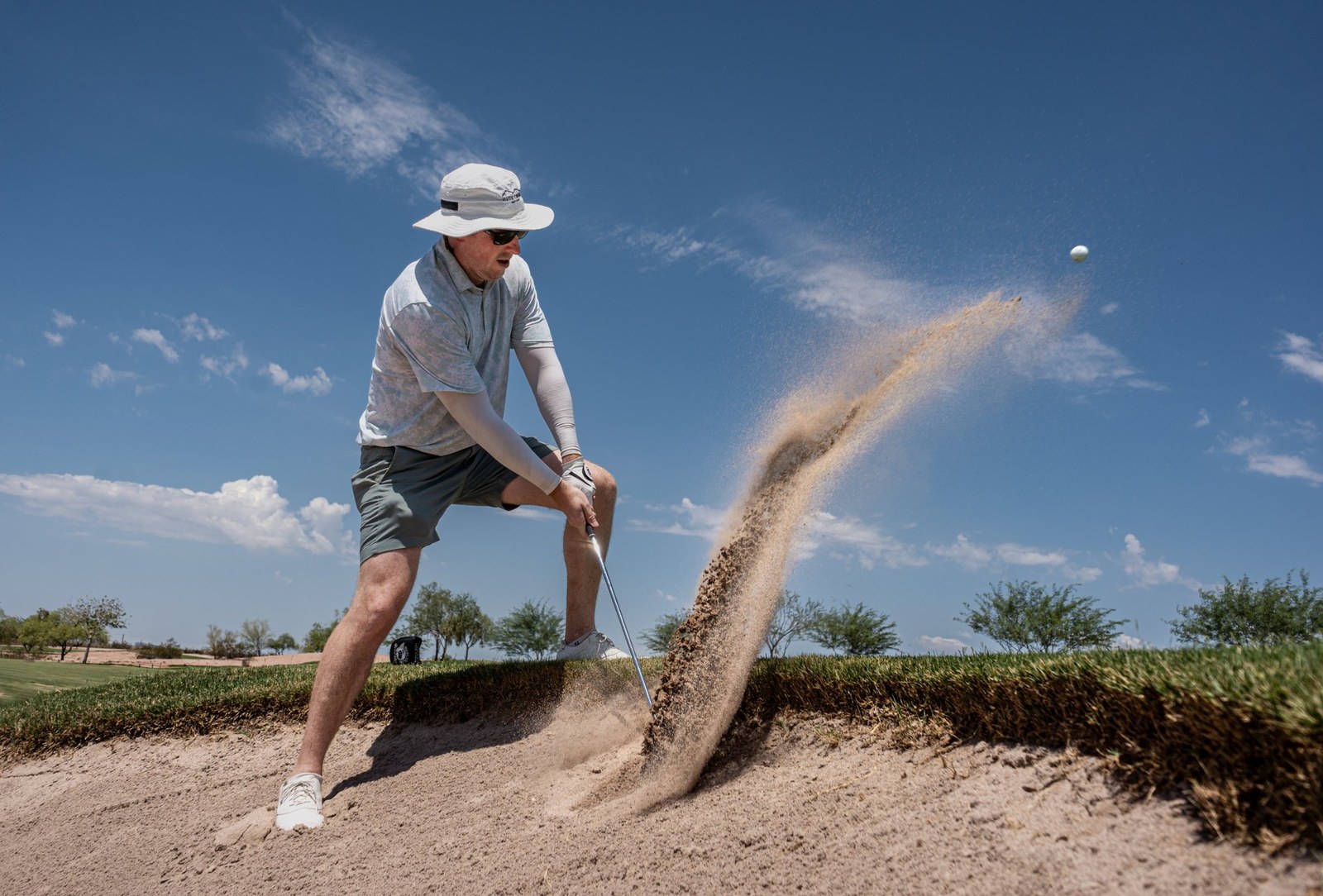 Golfer blasting out of a bunker, sand spraying toward the ball in the air