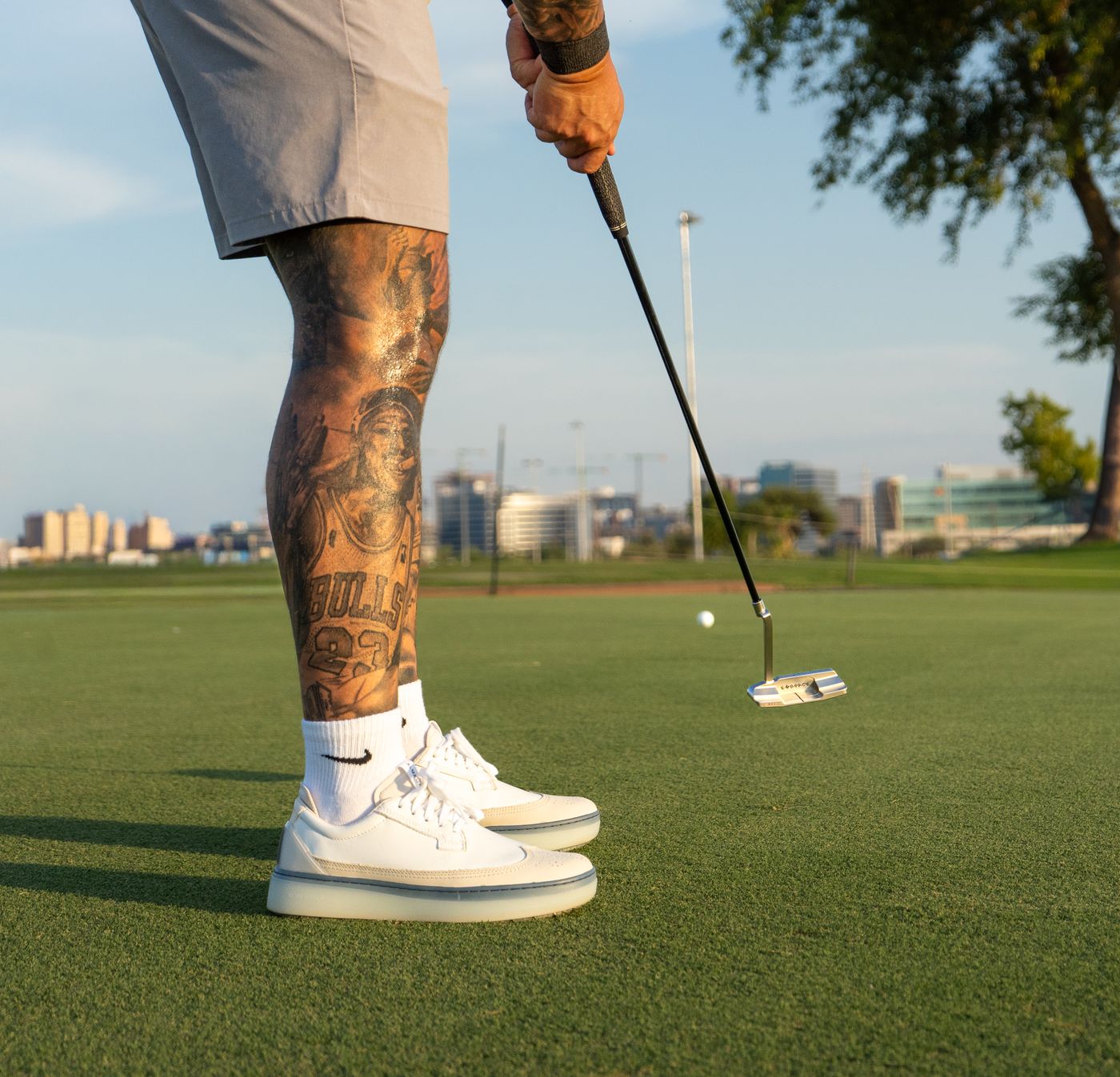 Close-up of a tattooed golfer’s legs and putter mid-stroke