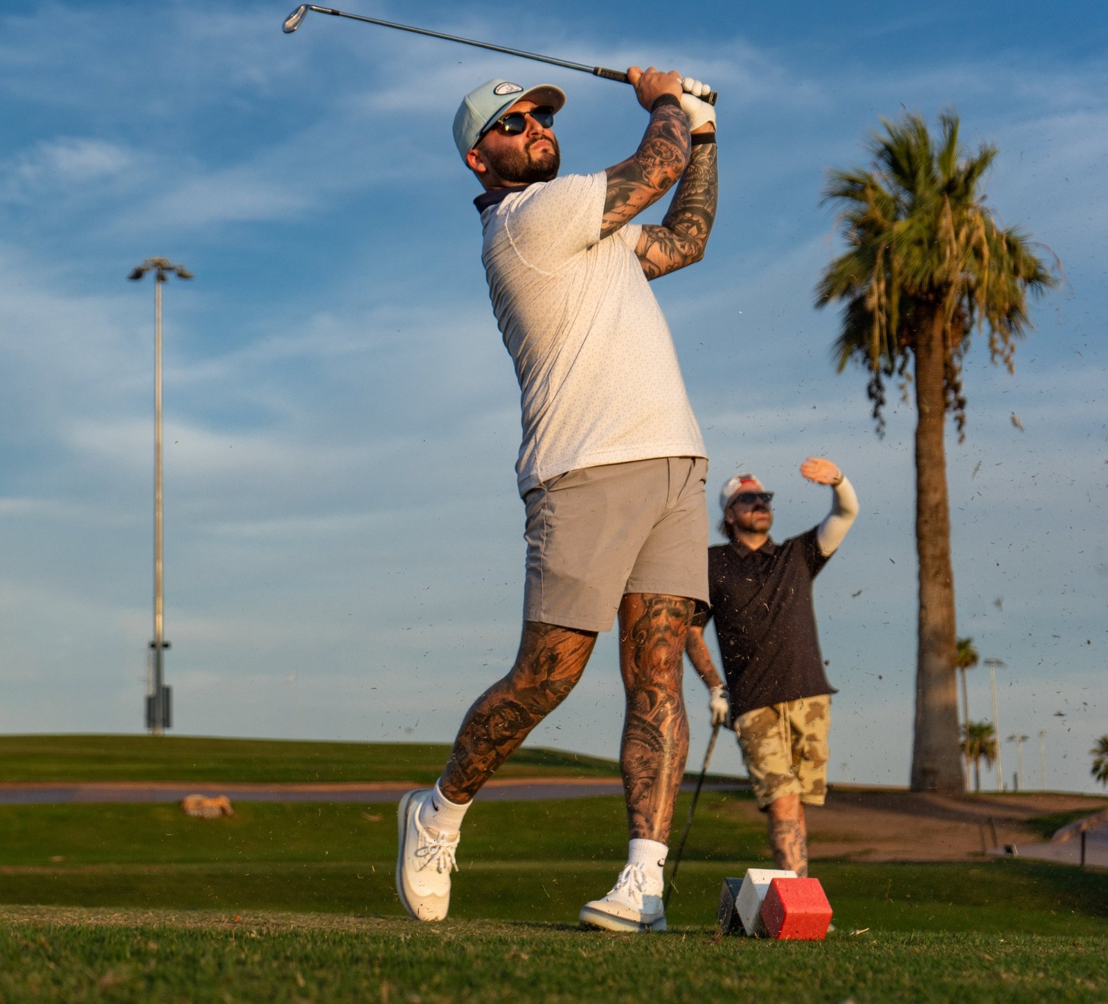 Golfer holding his finish as a playing partner shades his eyes behind him