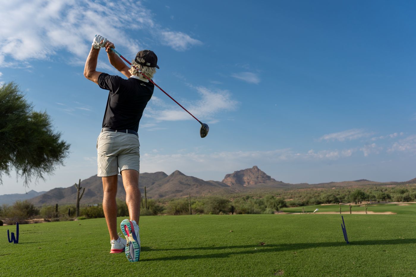 Golfer at the top of his finish with desert mountains down the fairway