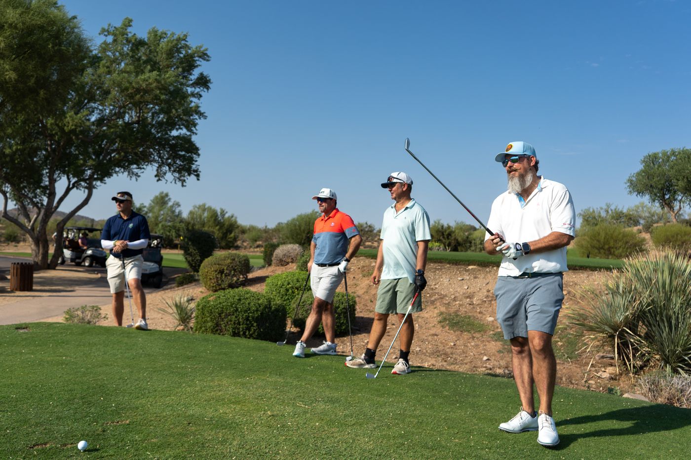 A group waiting on the tee box while one player watches his shot