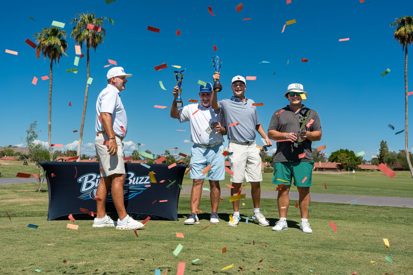 Tournament winners raising trophies as confetti falls on the tee